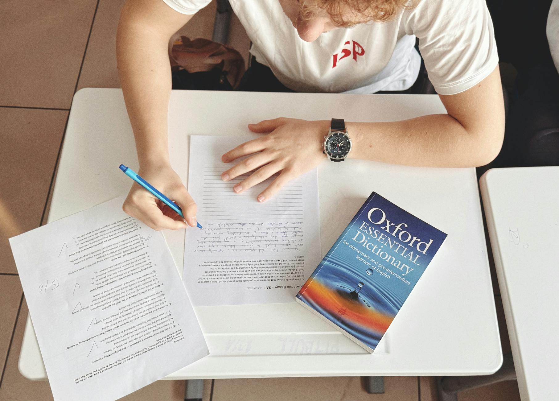 Student pisze test przy biurku z papierem i słownikiem Oxford