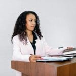 Zadania speaking na każdy dzień: 30 tematów, które rozruszają Twoją spontaniczność Czarnoskóra prawniczka przemawia przy mównicy z dokumentami i książkami