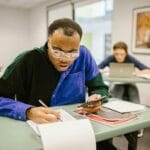 Studenci na egzaminie pisemnym w sali, skupieni na rozwiązywaniu testu