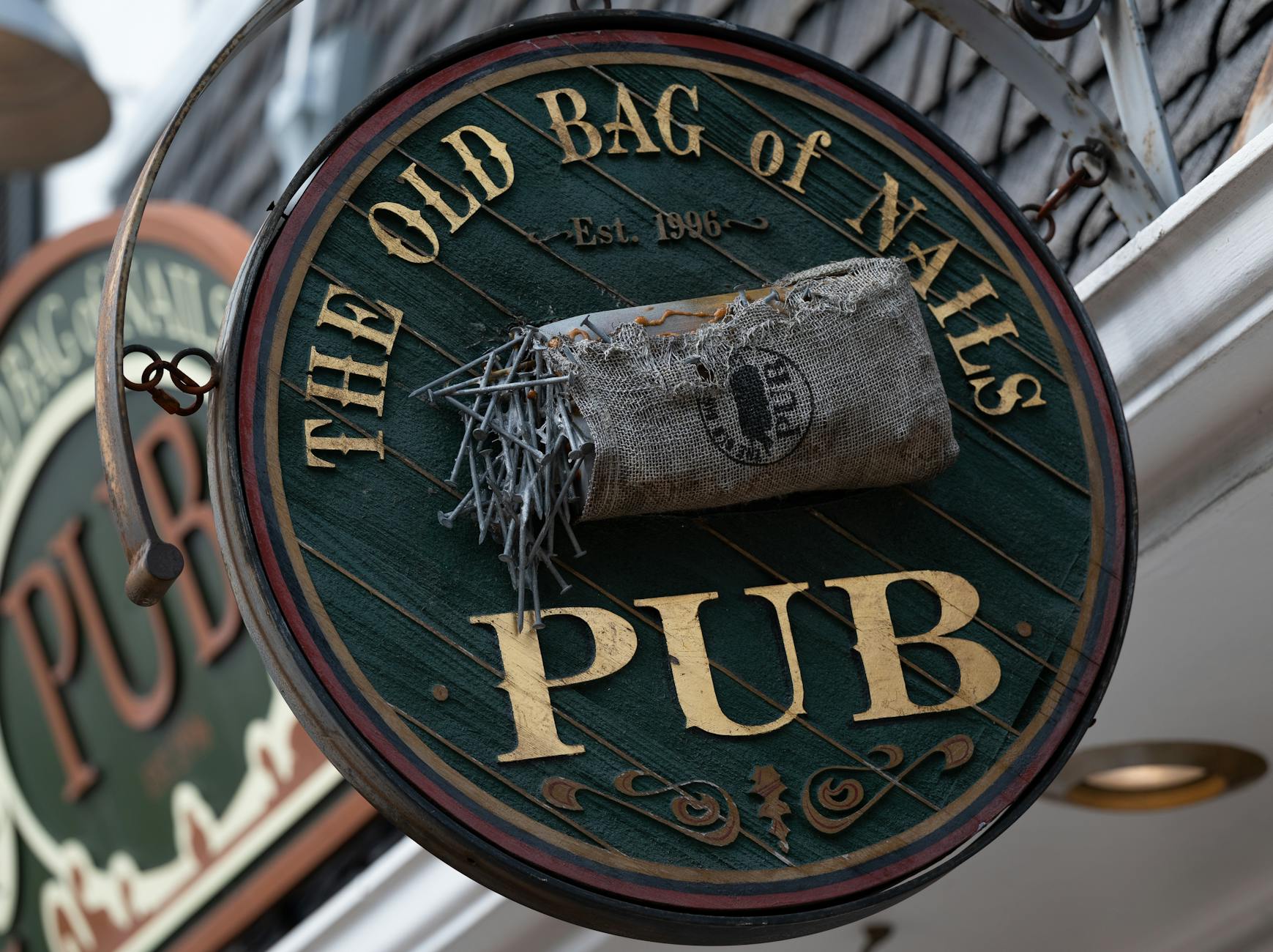 Etiykieta w pubie w Anglii: kolejka, płacenie i zwroty, które warto znać Szyld angielskiego pubu The Old Bag of Nails z ozdobnymi gwoździami