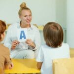 Jak czytać zapis fonetyczny IPA bez bólu głowy Nauczycielka pokazuje kartę z literą dzieciom w przedszkolnej sali