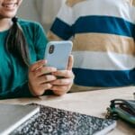 Jak używać aplikacji do powtórek (SRS) pod maturę i Cambridge: gotowe ustawienia Uśmiechnięta uczennica przy szkolnej ławce pokazuje coś na smartfonie