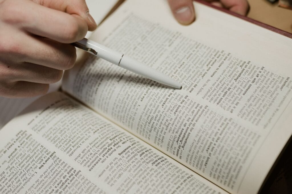 Dłoń wskazująca długopisem tekst w otwartej książce