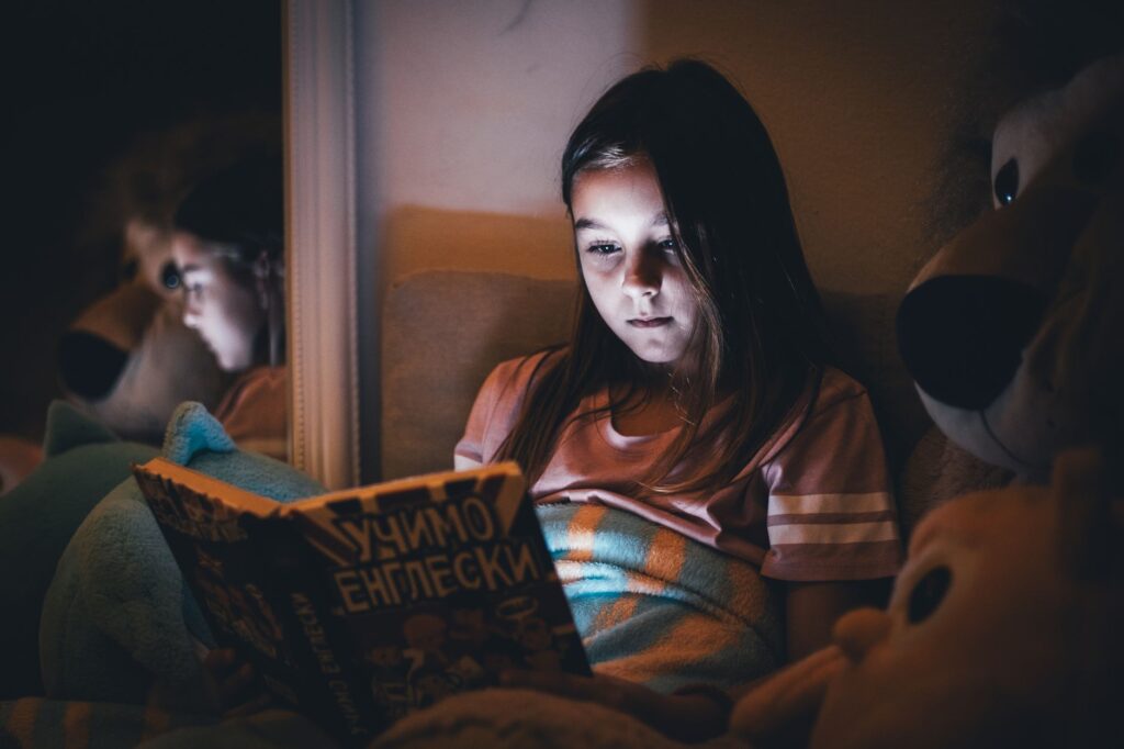 Dziewczynka czyta książkę przy lampce nocnej w przytulnym pokoju